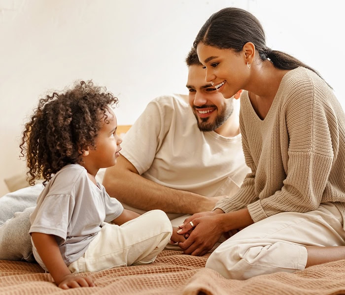 Parents souriants discutant avec leur jeune enfant assis sur un lit